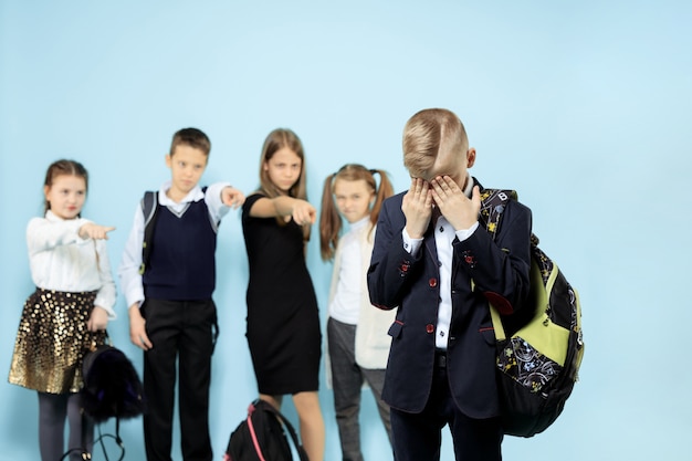 Little boy standing alone and suffering an act of bullying while children mocking