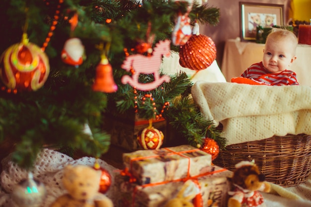 Little boy in stripped pyjamas sits before a Christmas tree 