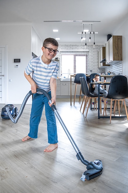 A little boy with glasses cleans the house with a vacuum cleaner.