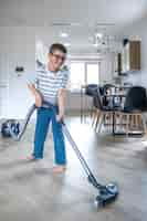 Free photo a little boy with glasses cleans the house with a vacuum cleaner.