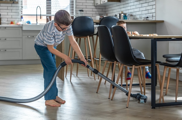 A little boy with glasses cleans the house with a vacuum cleaner.