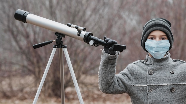 Little boy with medical mask using a telescope