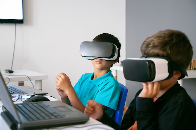 Free photo little boys using vr headset and sitting at table with laptop