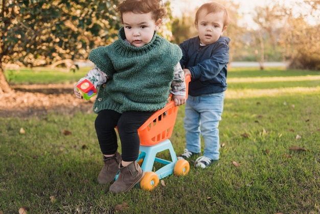 Little brother and sister playing with toy cart in garden