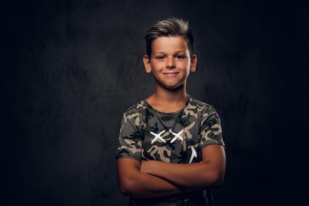 Little charming boy with nice hairstyle is posing over dark background at photo studio.