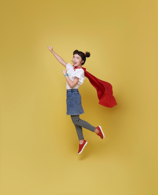 Free photo little child asian girl plays superhero flying back to school isolated on yellow background