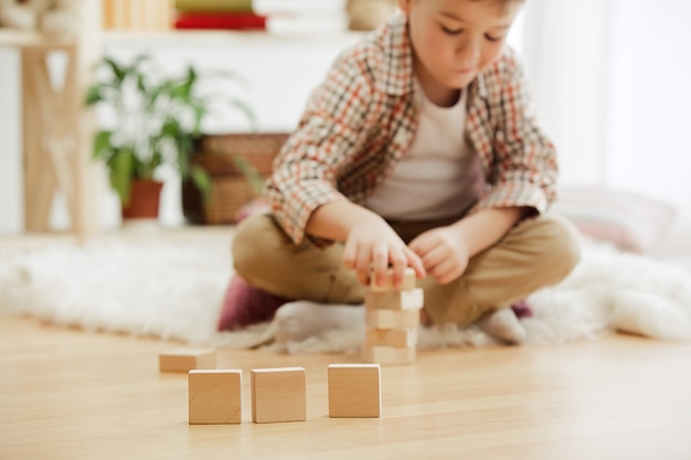 Little child sitting on the floor. Pretty boy palying with wooden cubes at home. Conceptual image with copy or negative space and mock-up for your text