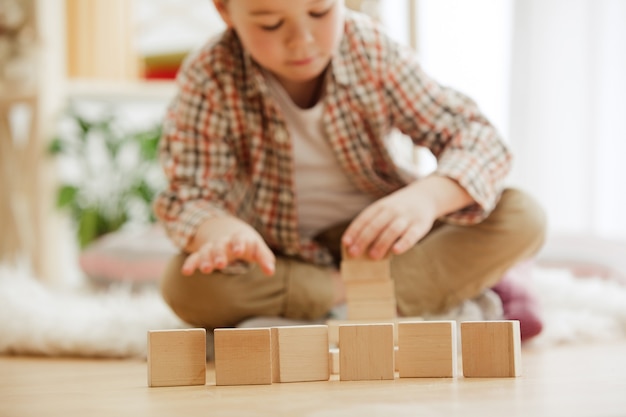 Free Photo little child sitting on the floor. pretty boy palying with wooden cubes at home. conceptual image with copy or negative space and mock-up for your text