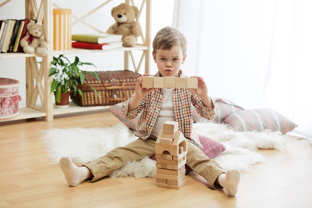 Little child sitting on the floor. Pretty boy palying with wooden cubes at home. Conceptual image with copy or negative space and mock-up for your text