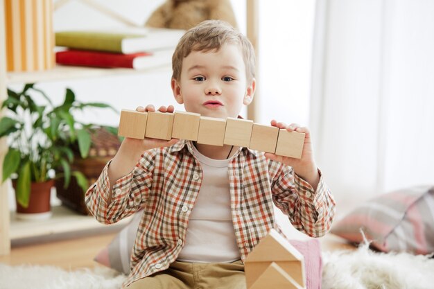 Little child sitting on the floor. Pretty boy palying with wooden cubes at home.