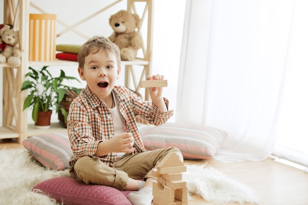 Free photo little child sitting on the floor. pretty smiling surprised boy palying with wooden cubes at home. conceptual image with copy or negative space and mock-up for your text.