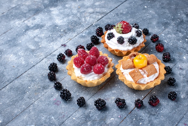 Free photo little creamy cakes with raspberries along with heart shaped blackberries on bright desk, fruit berry cake biscuit