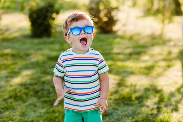 Little cute boy looks surprised in summer garden in bright sunglasses.