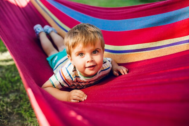 Little cute boy resting on bright hammock and looks relaxed.