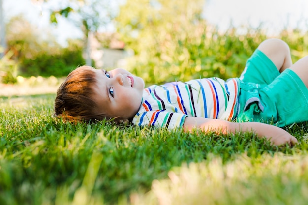 Free Photo little cute boy resting on the green grass in the garden and looks happy and relaxed.