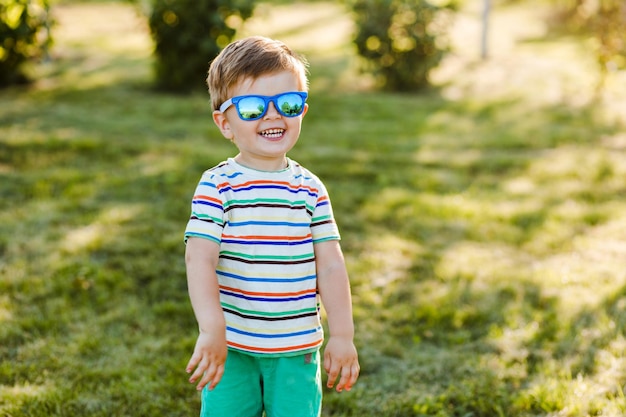 Little cute boy smiles in summer garden in bright sunglasses and shows his happiness .