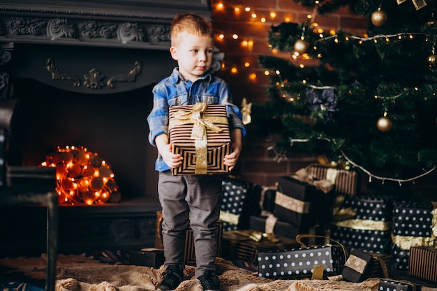 Little cute boy with christmas gift by Christmas tree