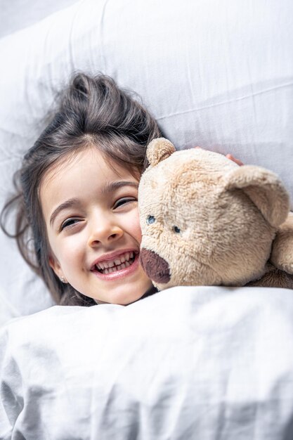 Little cute girl in bed with a teddy bear early in the morning