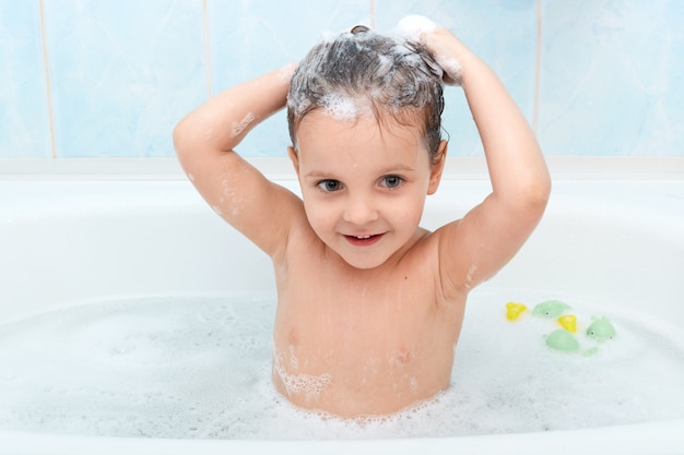 Little cute girl taking bath, washing her hair with shampoo by herself