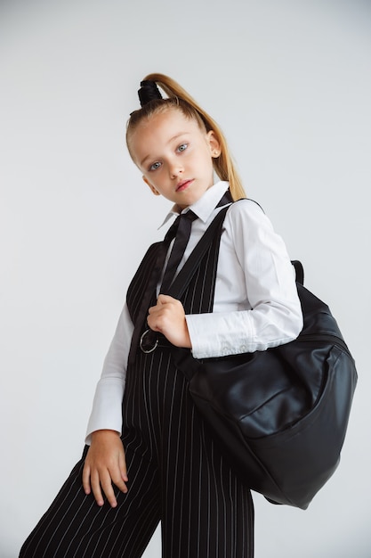 Free photo little female caucasian model posing in school's uniform with backpack on white background.