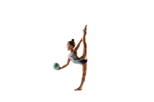 Little flexible girl isolated on white  wall. Little female model as a rhythmic gymnastics artist in bright leotard. Grace in motion, action and sport. Doing exercises with the ball.