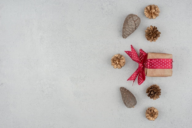 A little gift box with red bow and many of pinecones on white background