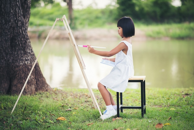 Free photo little girl artist painting picture in the park