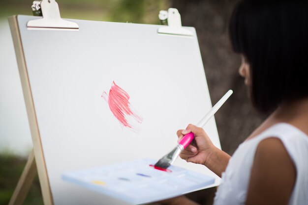 Little girl artist painting picture in the park