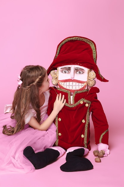 A little girl as beauty ballerina at pink long dress with nutcracker at pink studio