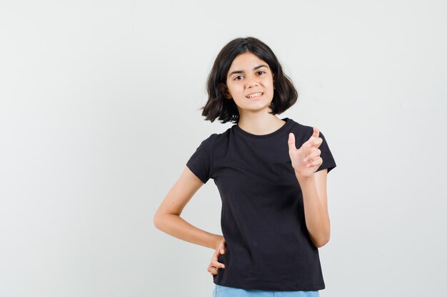 Little girl in black t-shirt, shorts showing small size sign and looking positive , front view.