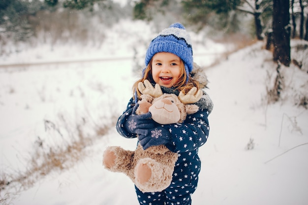 Little girl in a blue hat playing in a winter forest