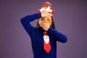 Free photo little girl in blue turtleneck with red tie and  funny christmas rim on head worried with hand on her forehead and c