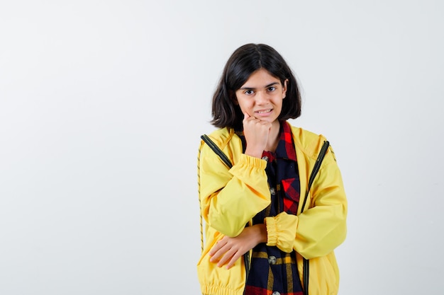 Little girl in checked shirt, jacket leaning chin on fist and looking cute 