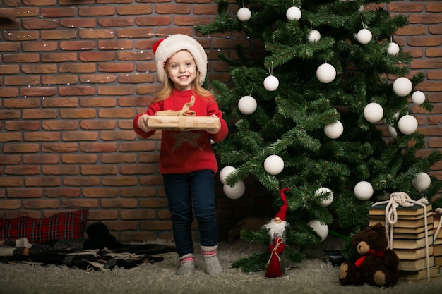 Free photo little girl on christmas with gift box by the christmas tree