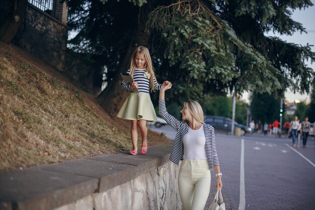 Little girl climbing a stone wall while grabbing her mother's hand