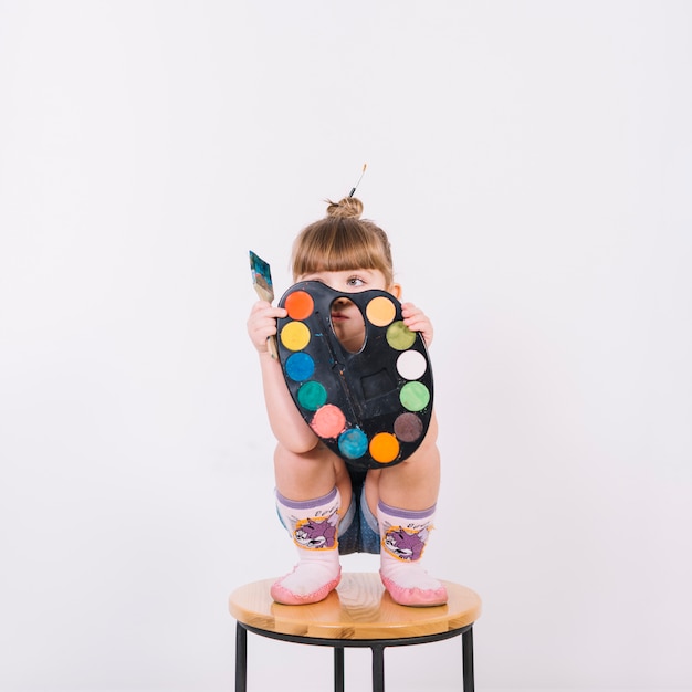 Free photo little girl covering face with palette on chair