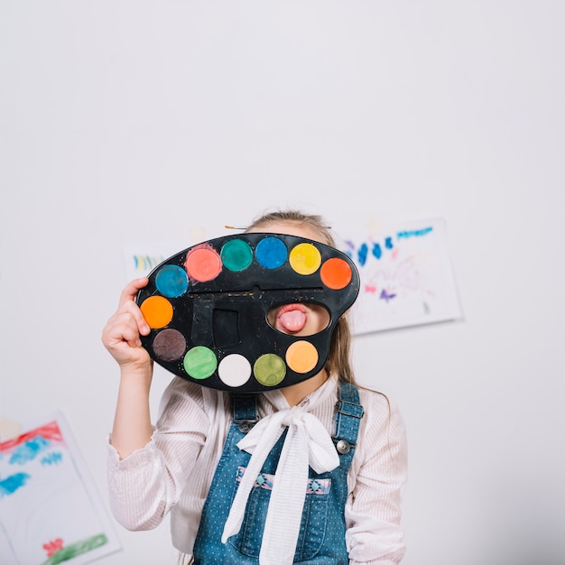 Free photo little girl covering face with palette and showing tongue