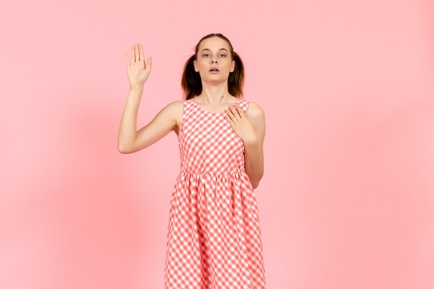 little girl in cute bright dress raising her hand on pink