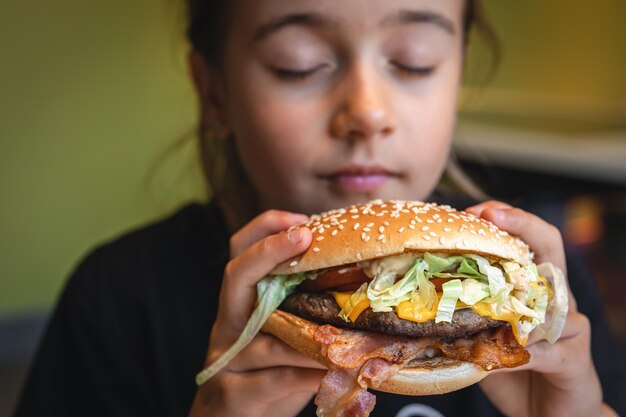 A little girl eats an appetizing burger closeup