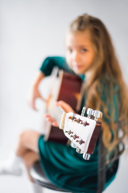 Free photo little girl in green dress playing acoustic guitar