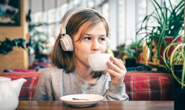 A little girl in headphones in a cafe with a cup of tea