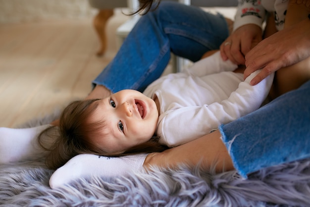 Little girl and her mom dressed in casual style have fun playing on the floor