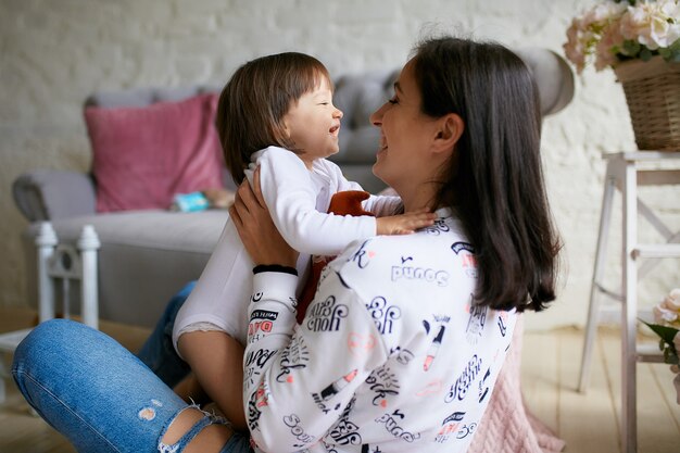 Little girl and her mom dressed in casual style have fun playing on the floor