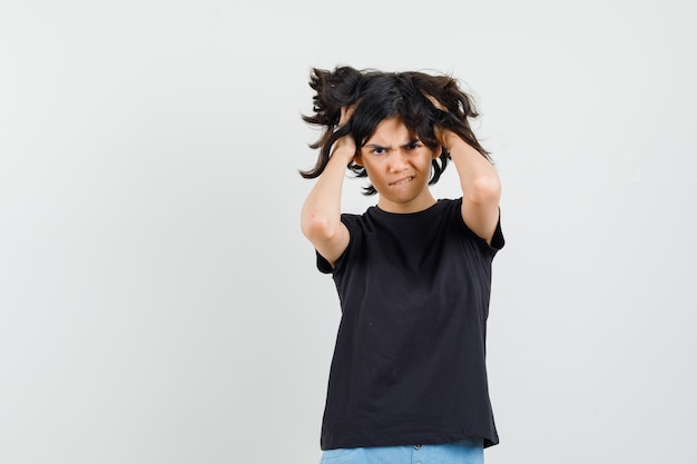 Free photo little girl holding hands in hair in black t-shirt, shorts and looking distressed , front view.