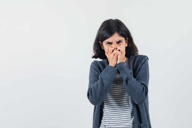 Little girl holding hands on mouth in t-shirt, jacket and looking helpless