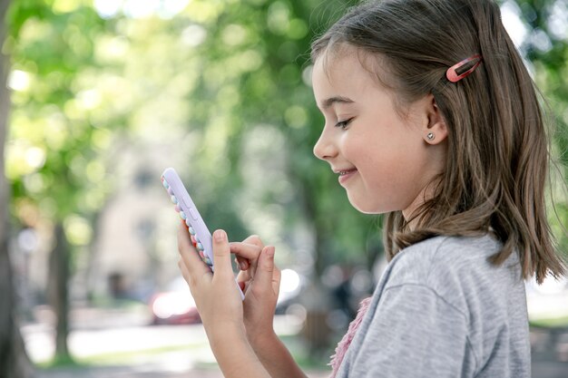 A little girl holds in her hand a phone in a case with pimples pop it, a trendy anti stress toy.