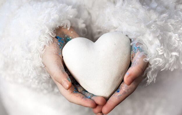 A little girl holds a white heart in her hands.