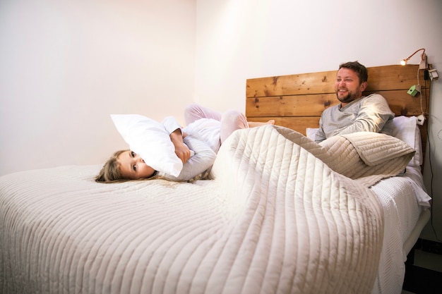 Little girl hugging a pillow on the bed next to her father