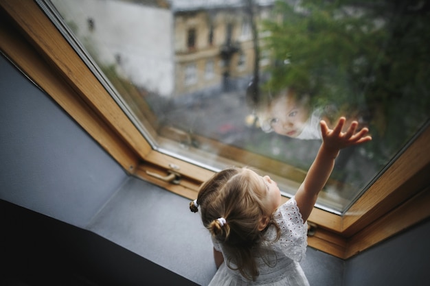 Free Photo little girl is looking out of the window