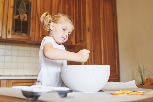 A little girl is preparing a dough for muffins.